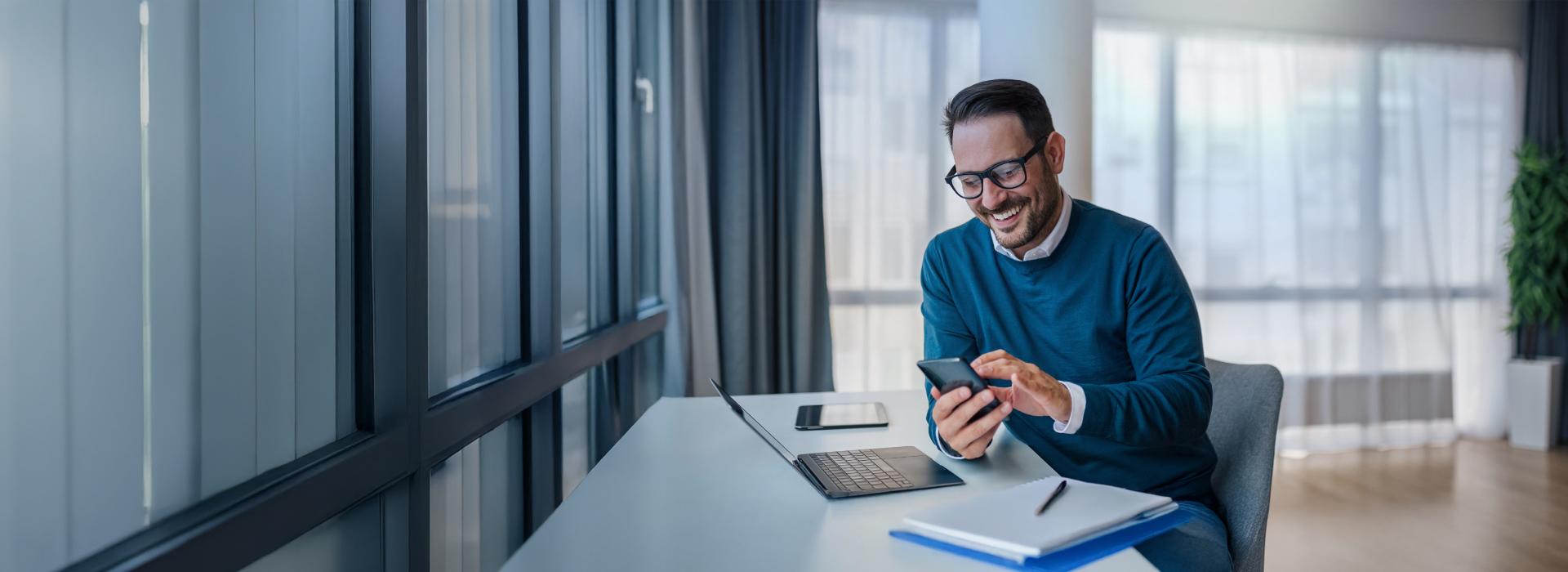 A man smiling looking at his mobile while working on his desk. Salary sacrifice end of FBT year 31 March. 