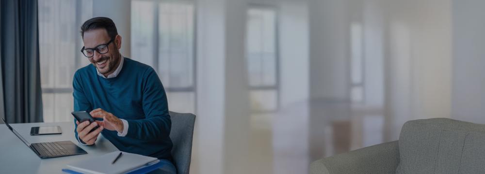 A man smiling looking at his mobile while working on his desk. Salary sacrifice end of FBT year 31 March. 